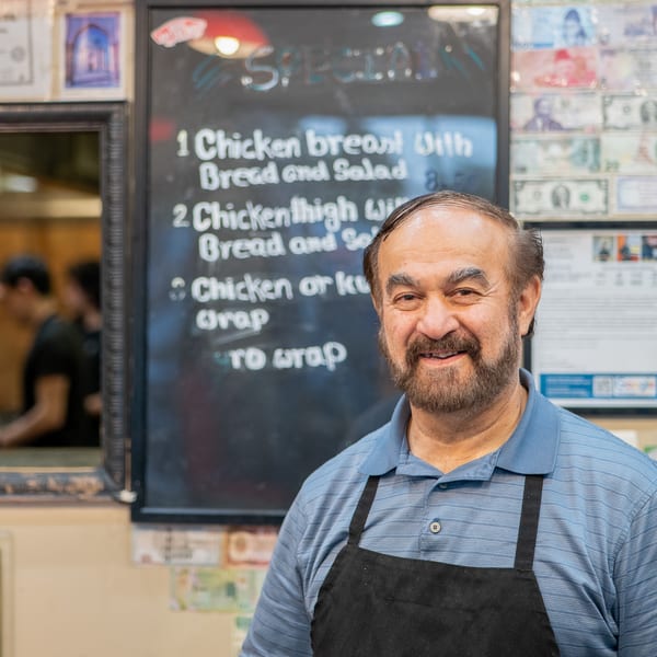 Smiling man in a blue polo and black apron stands in front of a specials board.