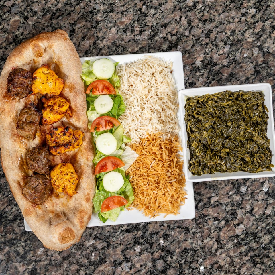 Grilled chicken and beef kebabs on flatbread with rice, salad, and a side of spinach.