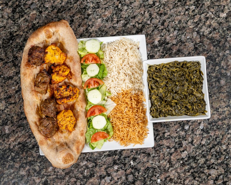 Grilled chicken and beef kebabs on flatbread with rice, salad, and a side of spinach.