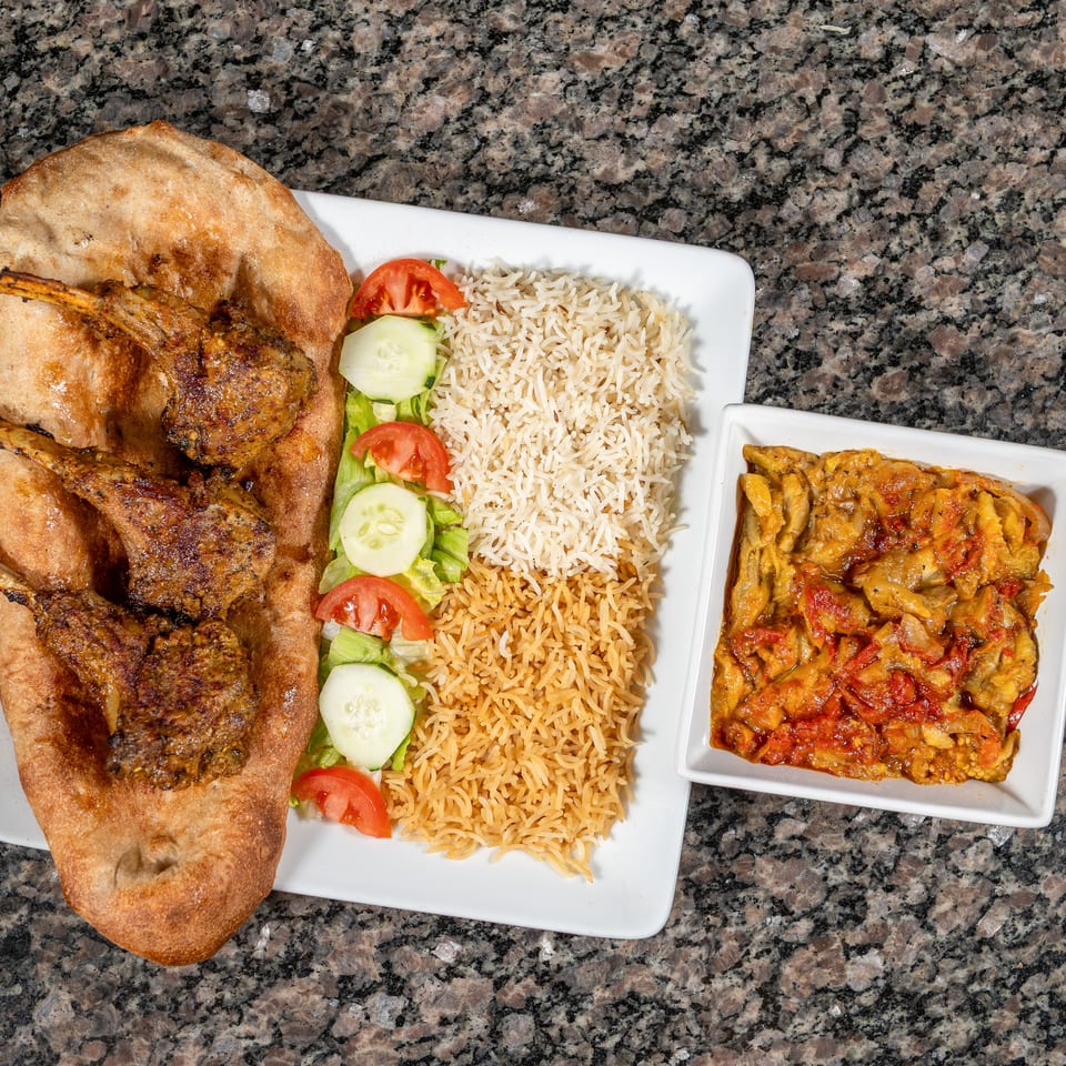 Grilled lamb chops on flatbread with rice, salad, and a side of stewed vegetables.