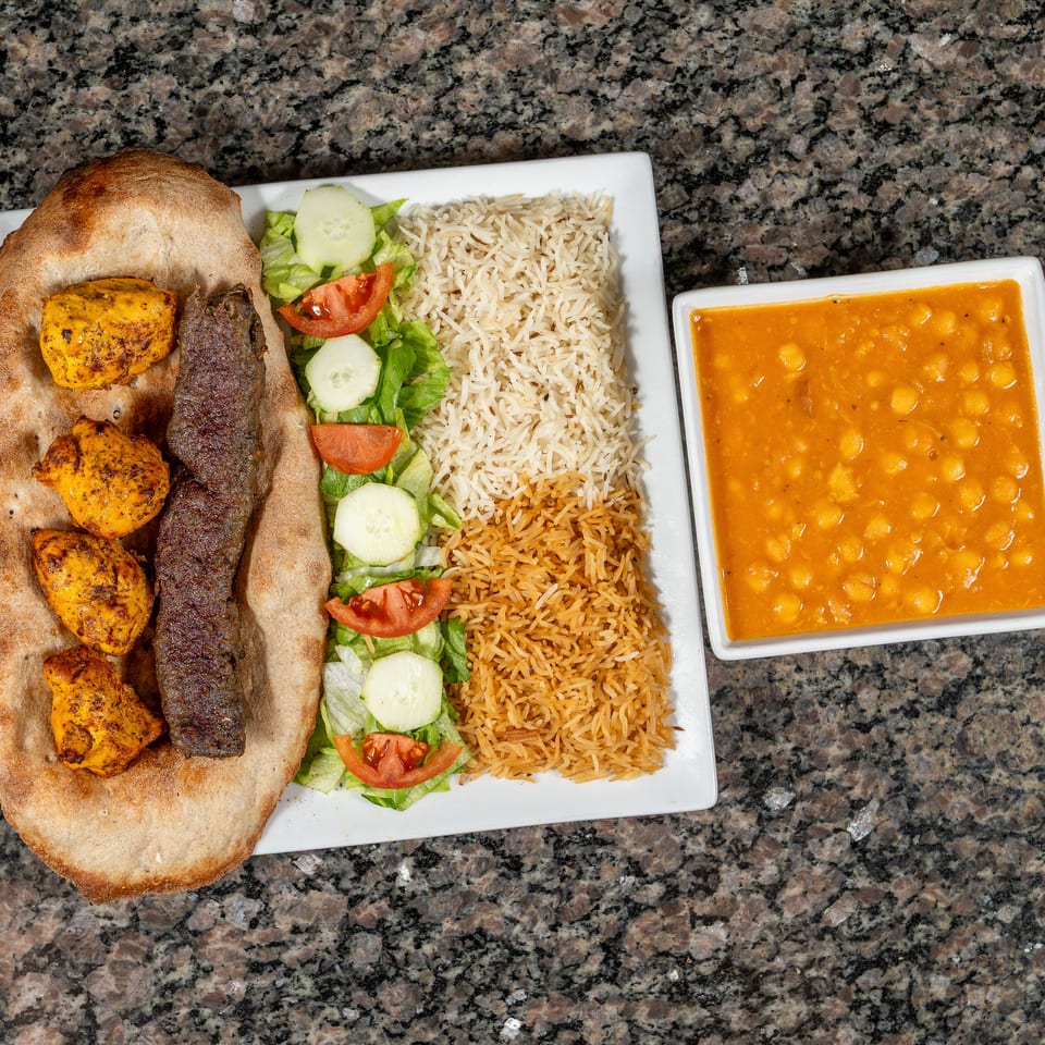 Platter with chicken and beef kebabs on naan, rice, salad, and a side of chickpea stew.