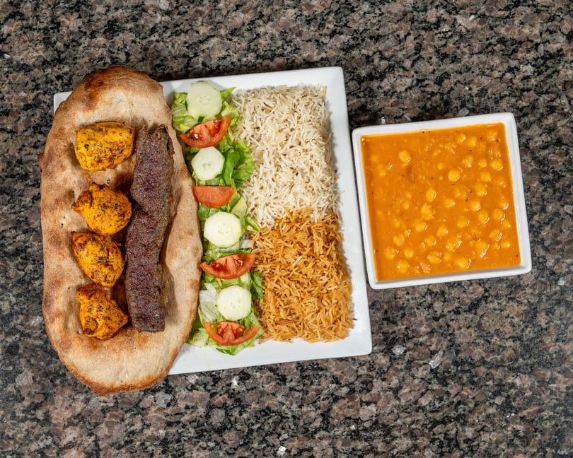 Platter with chicken and beef kebabs on naan, rice, salad, and a side of chickpea stew.