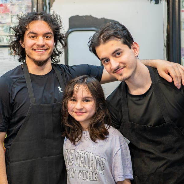 Two young men in black aprons and a young girl smiling at the camera.