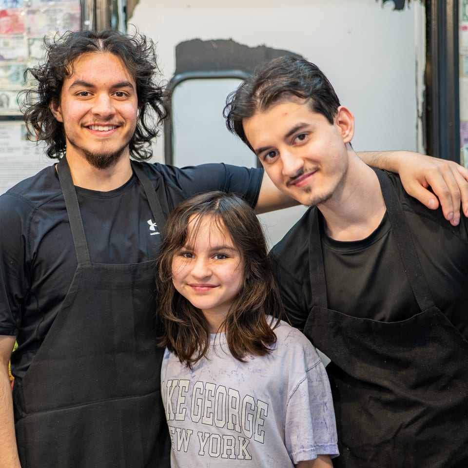 Two young men in black aprons and a young girl smiling at the camera.
