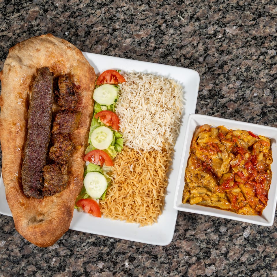 Grilled meat skewers on flatbread with rice, salad, and a side dish of stewed vegetables.