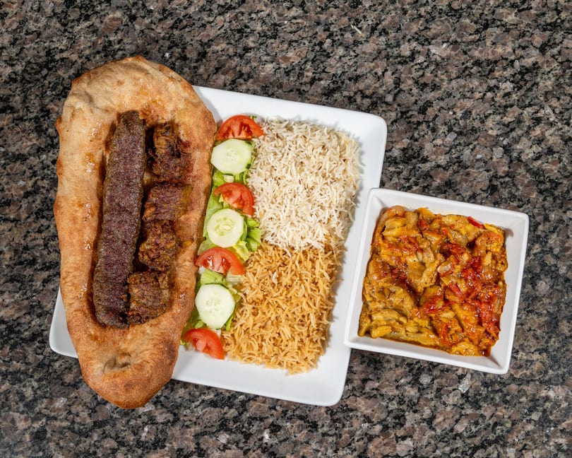 Grilled meat skewers on flatbread with rice, salad, and a side dish of stewed vegetables.