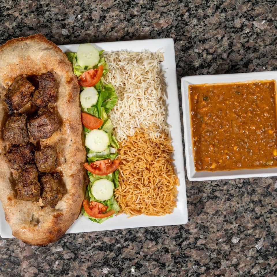 Grilled meat on flatbread, with rice, salad, and a side of lentil stew.