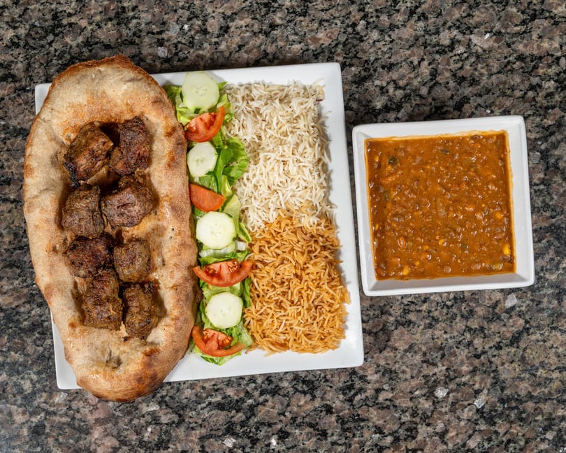 Grilled meat on flatbread, with rice, salad, and a side of lentil stew.
